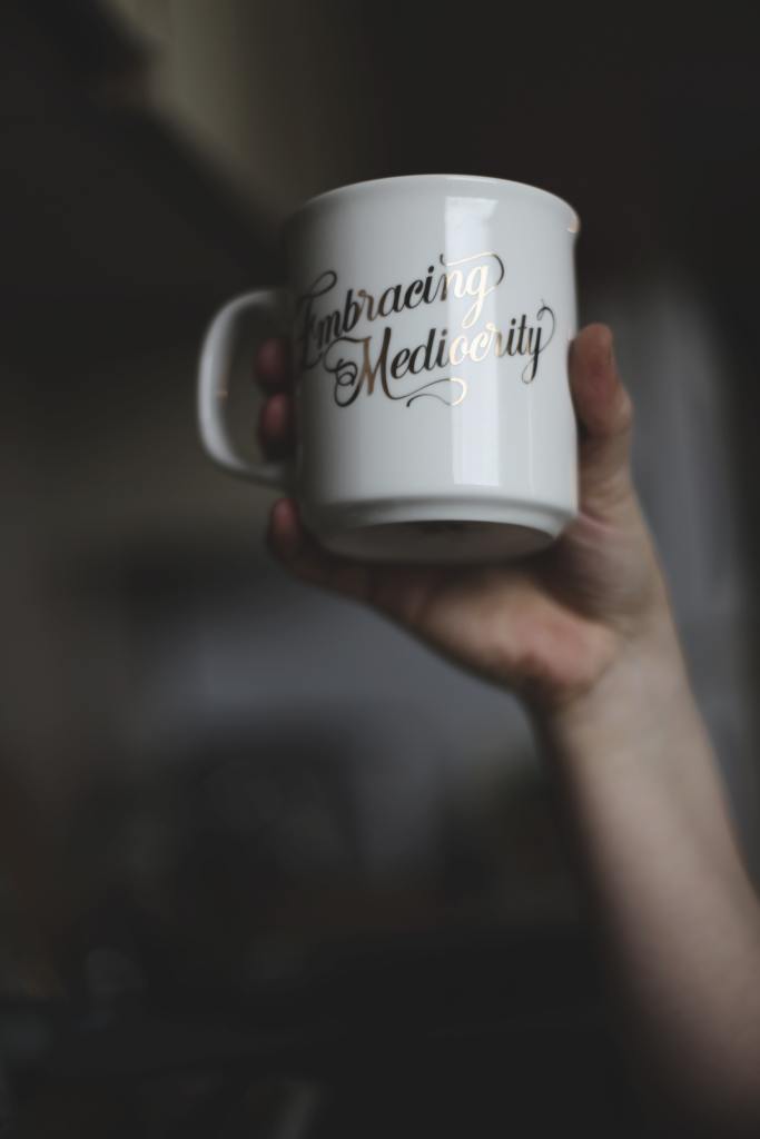 Hand holding a cup with the writing embracing mediocrity